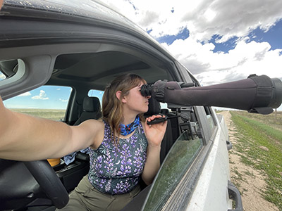 Emma Johnson looks through a scope mounted on a car window